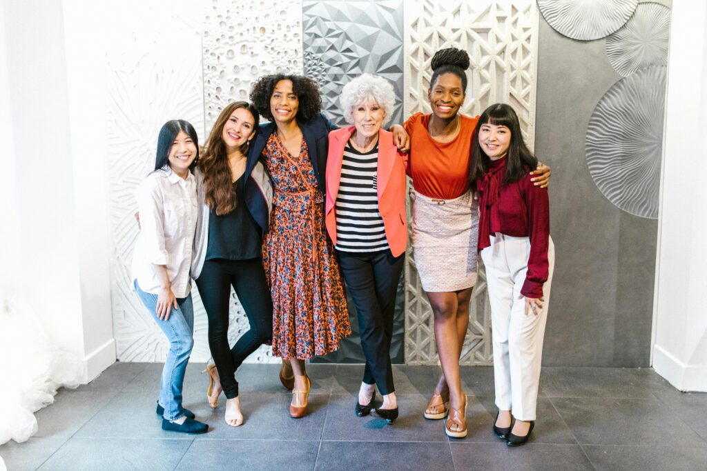 A joyful group of diverse women in stylish business attire posing together indoors.